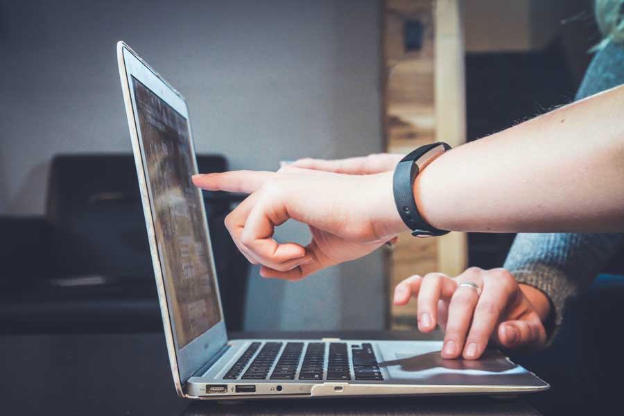 Laptop open with close up hands of users pointing to the screen during remote learning