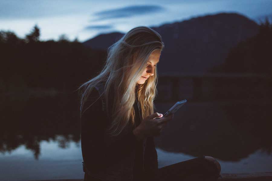 Woman outdoor in the dark near pond using her iphone.