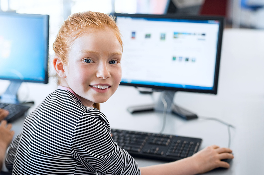 Young girl with red hair using computer at elementary school