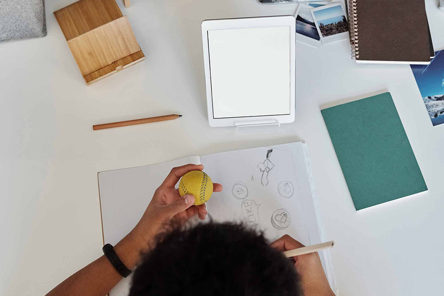 top view of student drawing while open tablet sits in front of them during distance learning